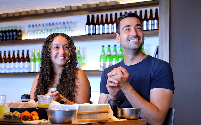Couple enjoying sushi with sake bottles in the background.