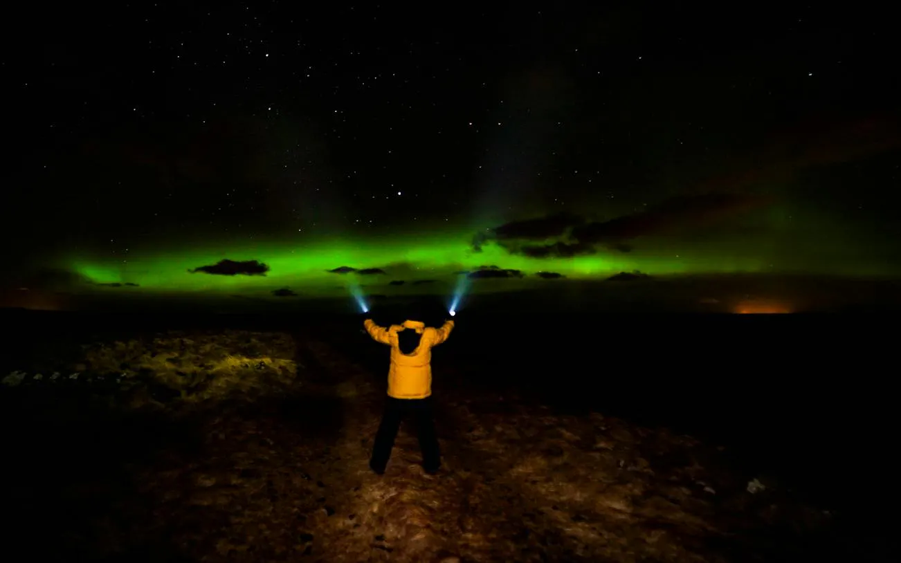 Person with flashlights under Northern Lights, Reykjavik tour.