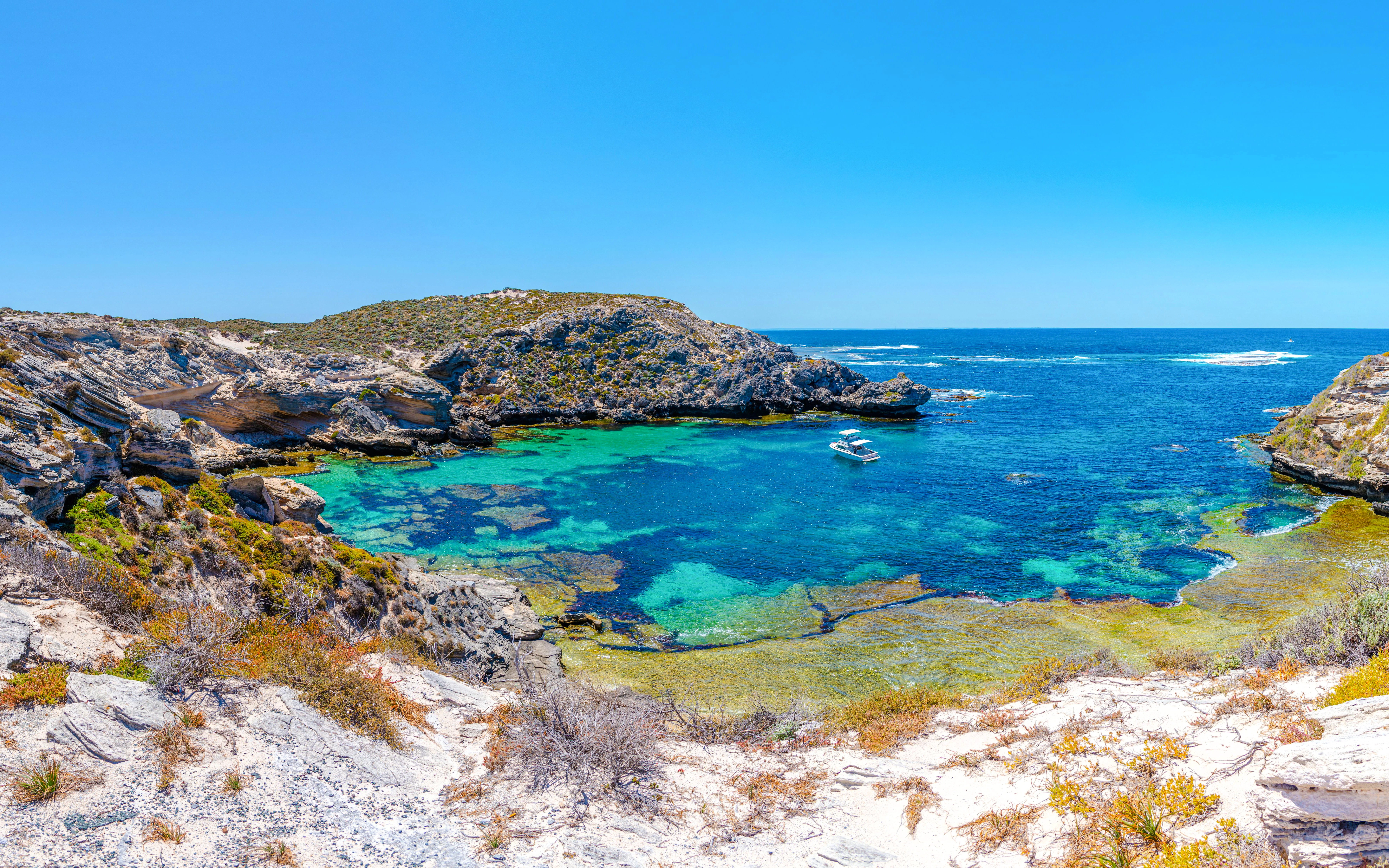 Boat anchored in turquoise waters of Fish Hook Bay, Rottnest Island, Australia, surrounded by rocky cliffs.