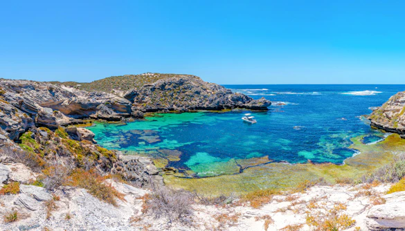 Boat anchored in turquoise waters of Fish Hook Bay, Rottnest Island, Australia, surrounded by rocky cliffs.