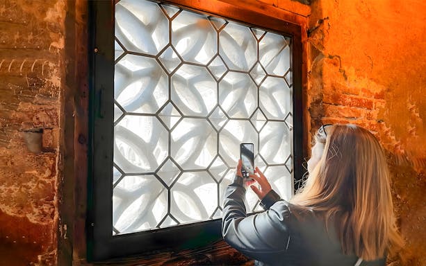 Lady photographing Bridge of Sighs through ornate window grille in Venice.