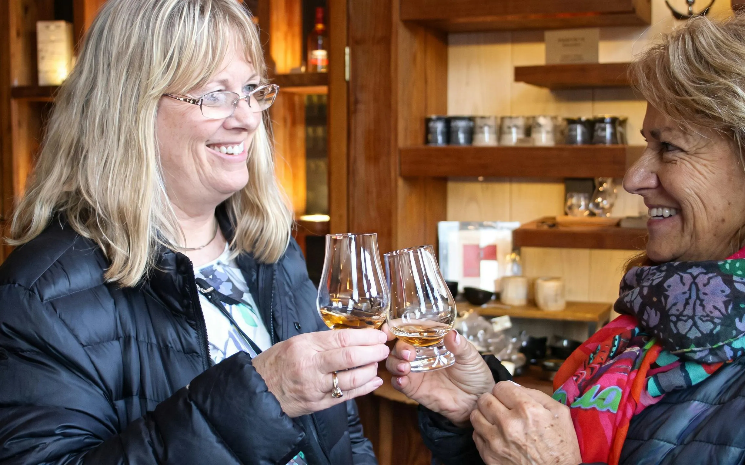 Women toasting with whisky glasses in a cozy tasting room.