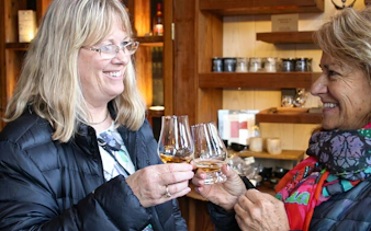 Women toasting with whisky glasses in a cozy tasting room.