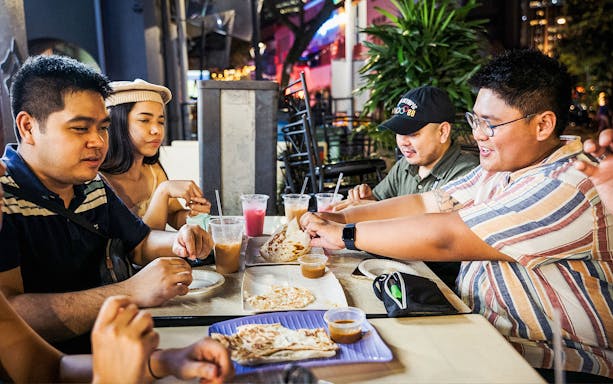 Group enjoying roti prata and drinks at a Singapore street food night market.