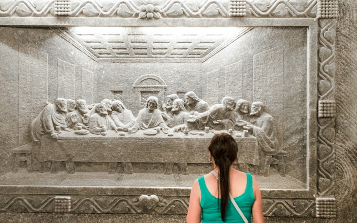 Visitor admiring salt carving of The Last Supper at Wieliczka Salt Mine.