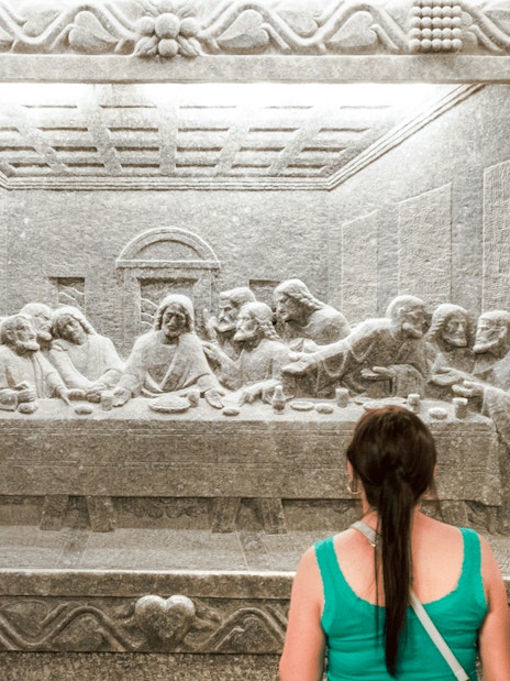 Visitor admiring salt carving of The Last Supper at Wieliczka Salt Mine.