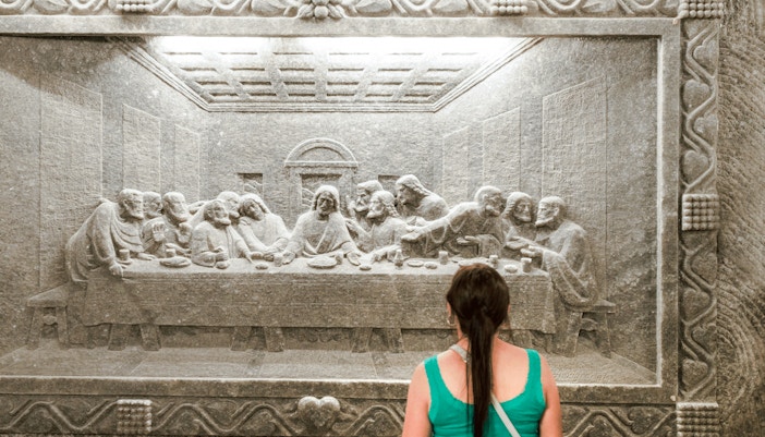 Visitor admiring salt carving of The Last Supper at Wieliczka Salt Mine.