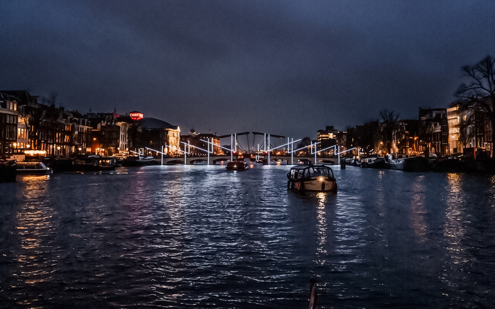 Amsterdam canal at night with illuminated bridge during Light Festival.