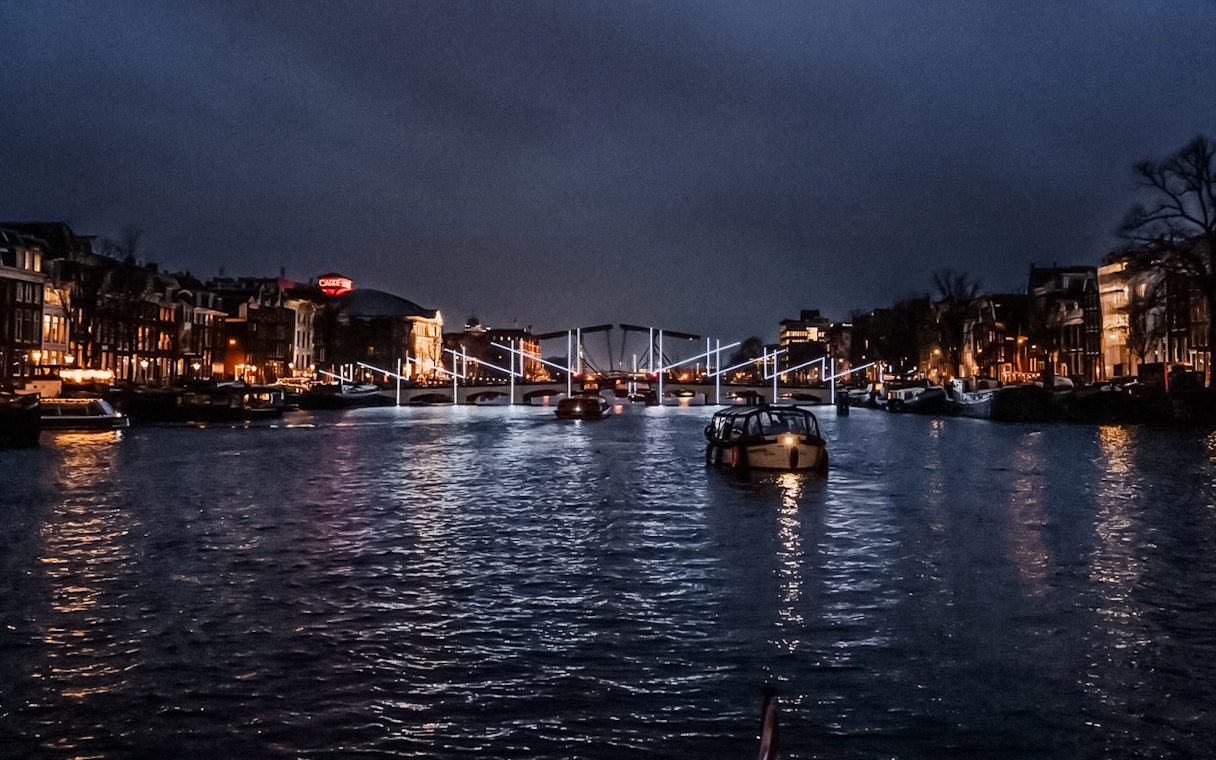 Amsterdam canal at night with illuminated bridge during Light Festival.