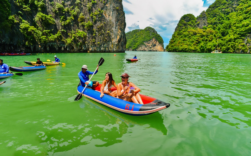 Tourists kayaking in Phang Nga Bay with limestone cliffs in the background.