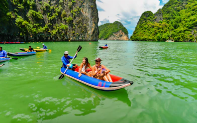 Tourists kayaking in Phang Nga Bay with limestone cliffs in the background.