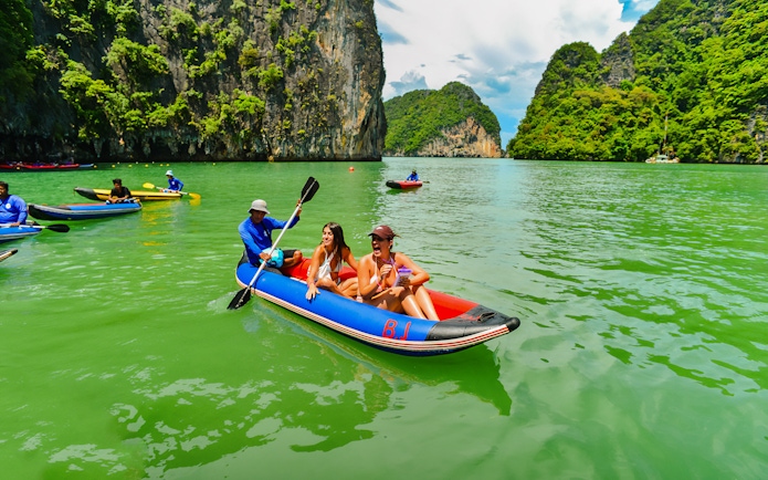 Tourists kayaking in Phang Nga Bay with limestone cliffs in the background.