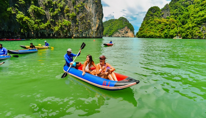 Tourists kayaking in Phang Nga Bay with limestone cliffs in the background.