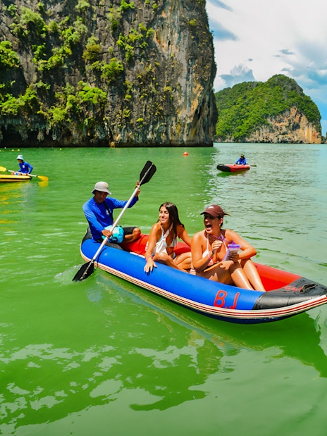 Tourists kayaking in Phang Nga Bay with limestone cliffs in the background.