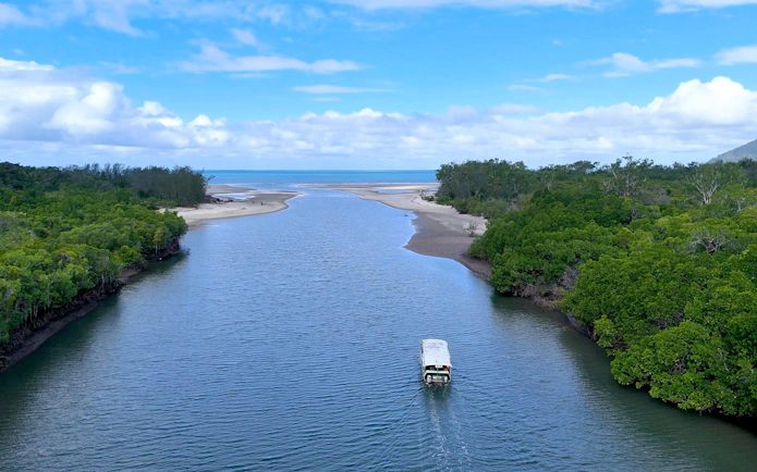 Tour boat on tropical river heading toward ocean, Daintree Rainforest, Australia.