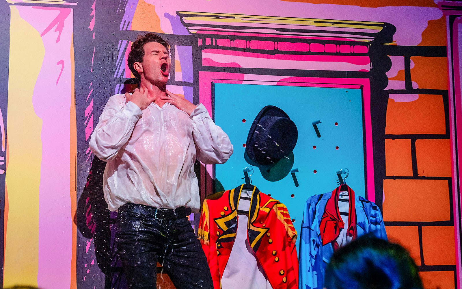 Performer in a wet shirt on stage with colorful costumes, related to Plied and Prejudice.