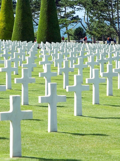 Rows of white crosses at Normandy American Cemetery, France, with visitors walking among them.