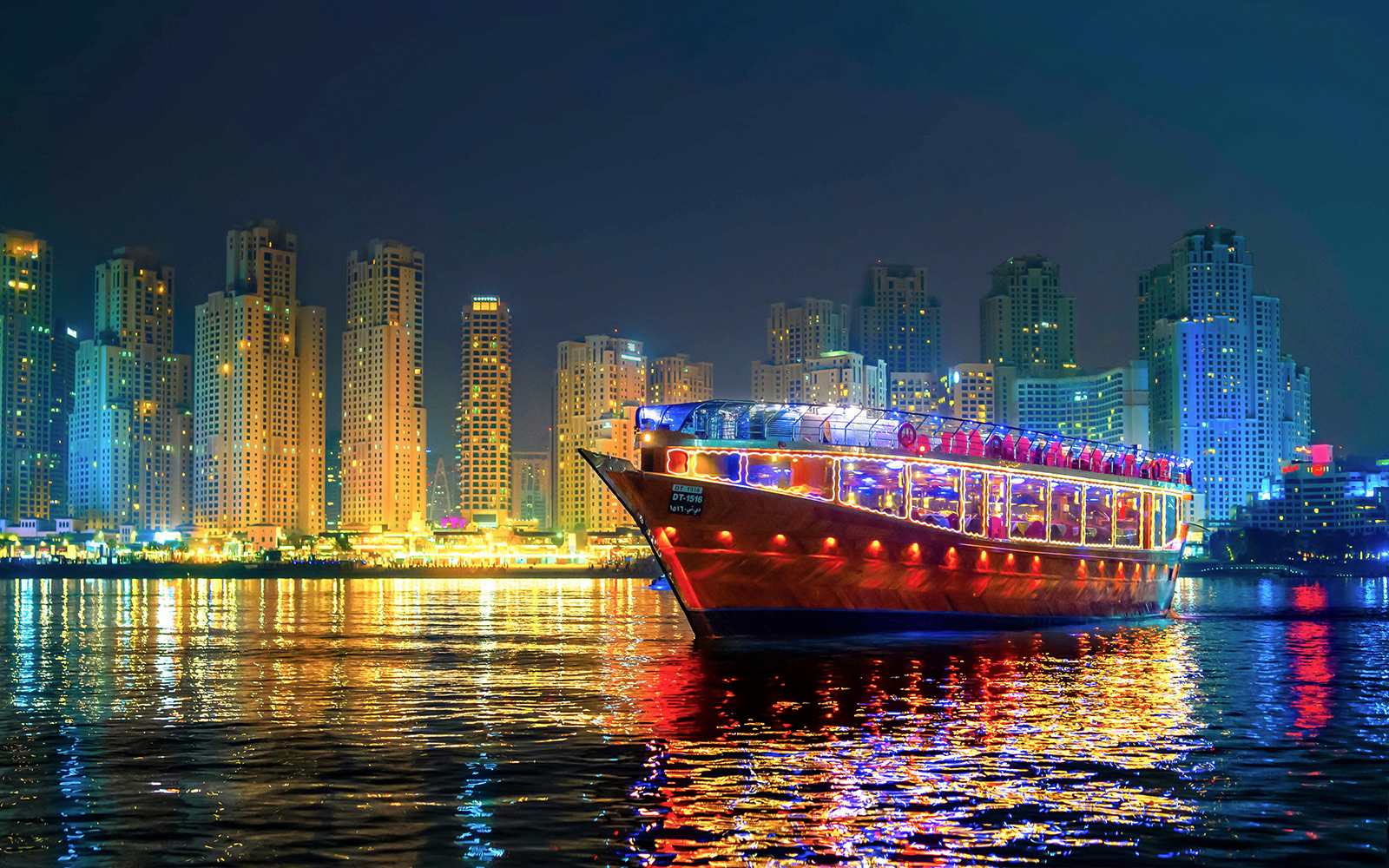 Luxury dhow cruise with lights on Dubai Marina at night, skyscrapers in the background.