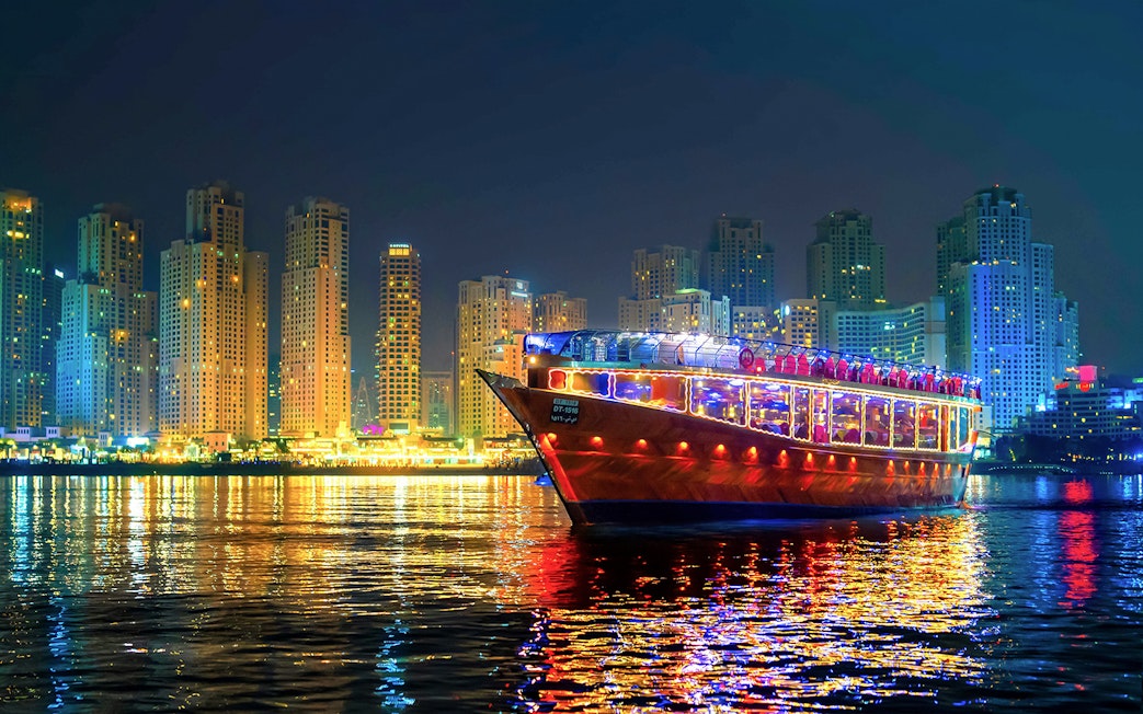 Luxury dhow cruise with lights on Dubai Marina at night, skyscrapers in the background.