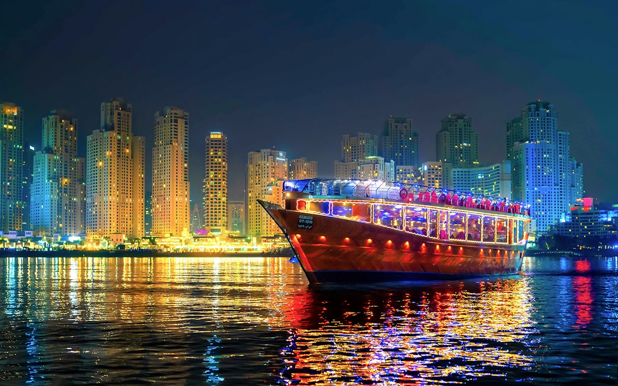 Luxury dhow cruise with lights on Dubai Marina at night, skyscrapers in the background.