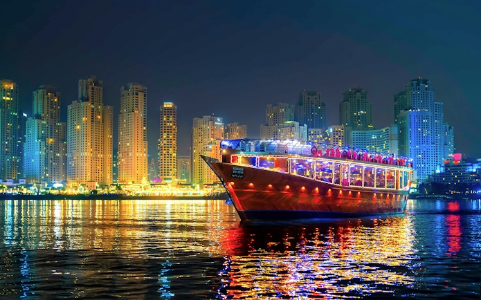 Luxury dhow cruise with lights on Dubai Marina at night, skyscrapers in the background.