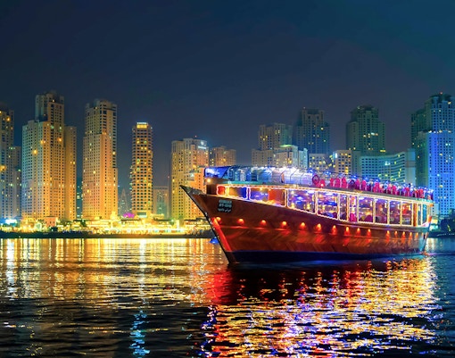 Luxury dhow cruise with lights on Dubai Marina at night, skyscrapers in the background.