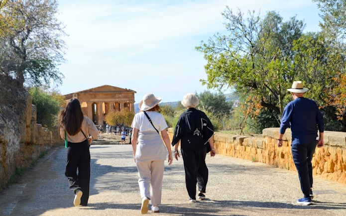 Visitors walking towards ancient temple ruins at Valley of Temples, Italy.