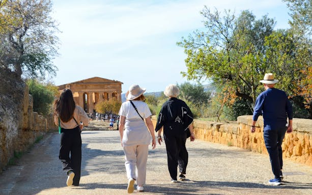 Visitors walking towards ancient temple ruins at Valley of Temples, Italy.