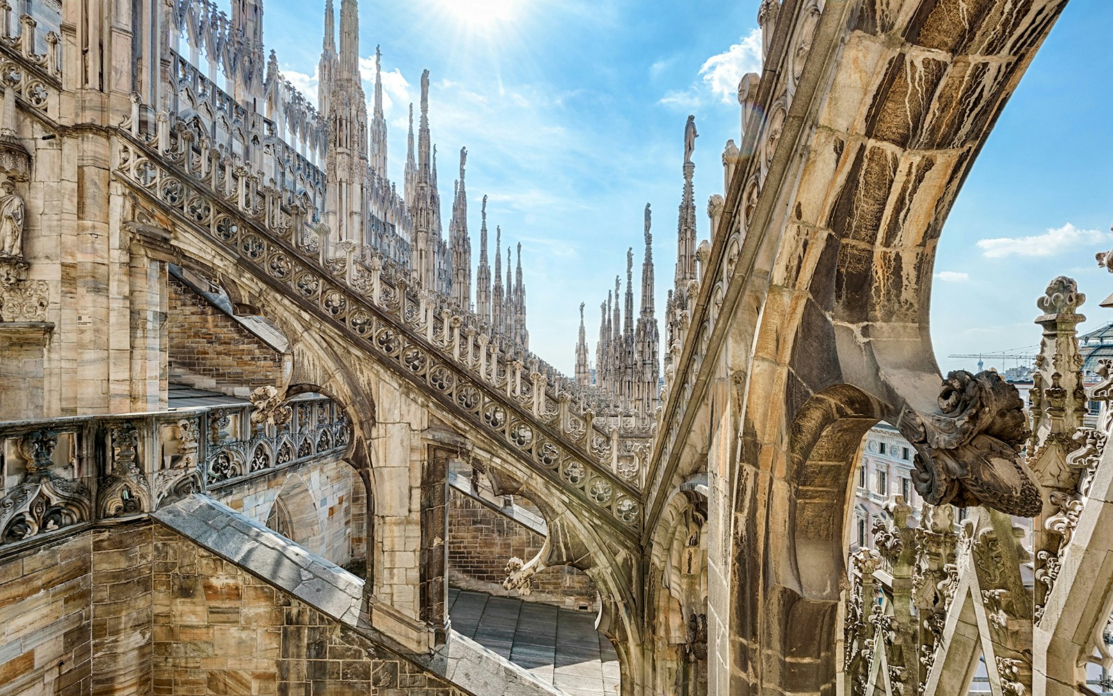 Milan Duomo rooftop with intricate spires and arches under a clear sky.
