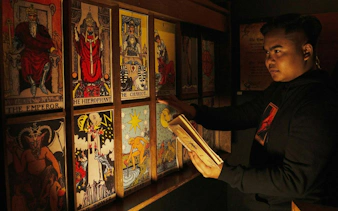 Person examining tarot cards in dimly lit room, Breakout Avenue K: Chamber of Hocus, Dubai.