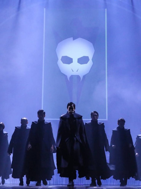 Cast performing on stage in "Harry Potter and the Cursed Child" with dark cloaks and a skull backdrop.