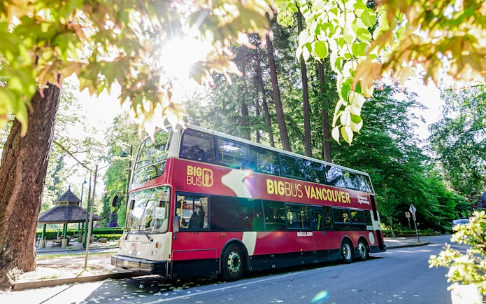 Big Bus Vancouver parked on a tree-lined street in a sunny park setting.