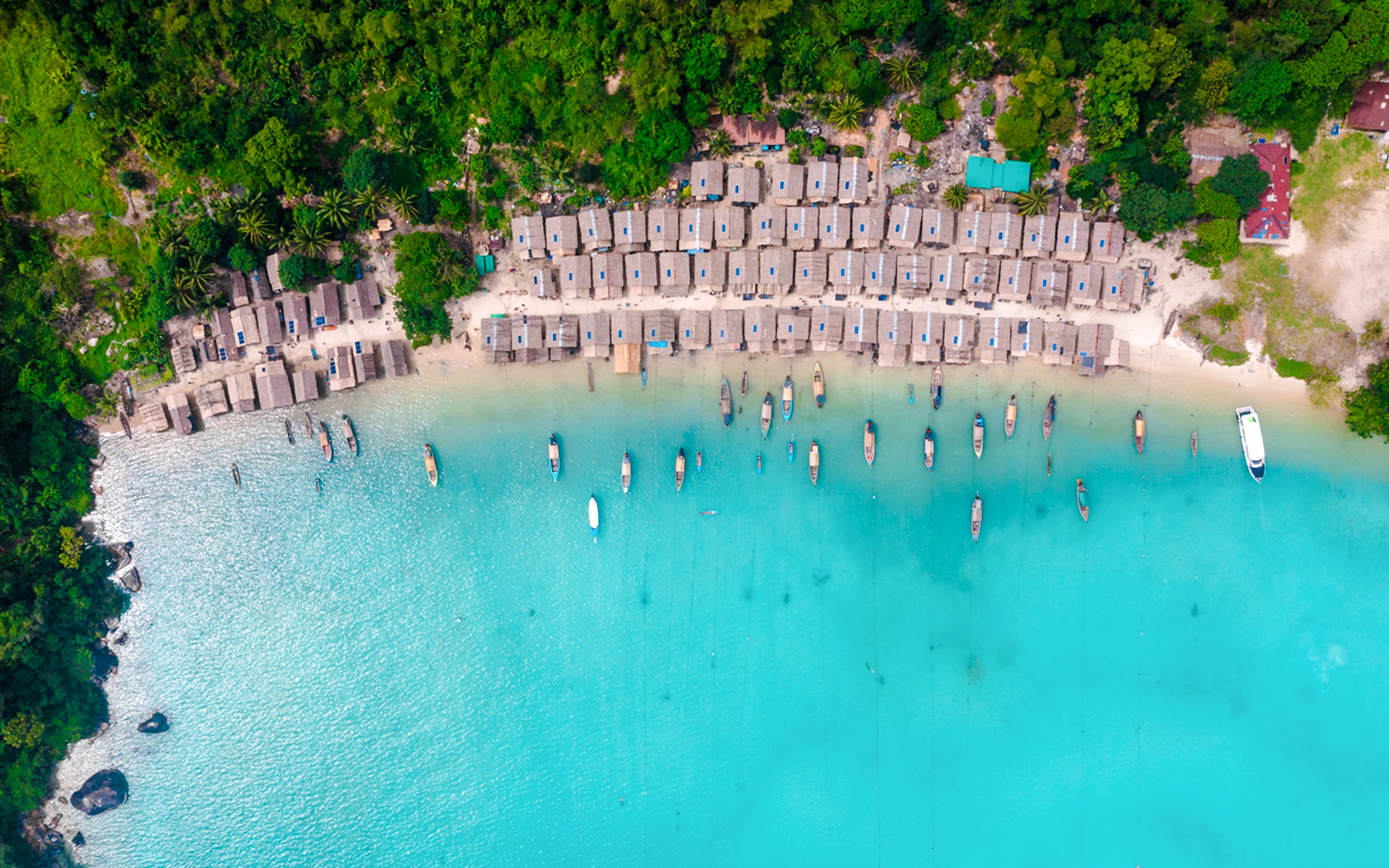 Aerial view of thatched-roof huts and boats along a bay in Surin Islands.
