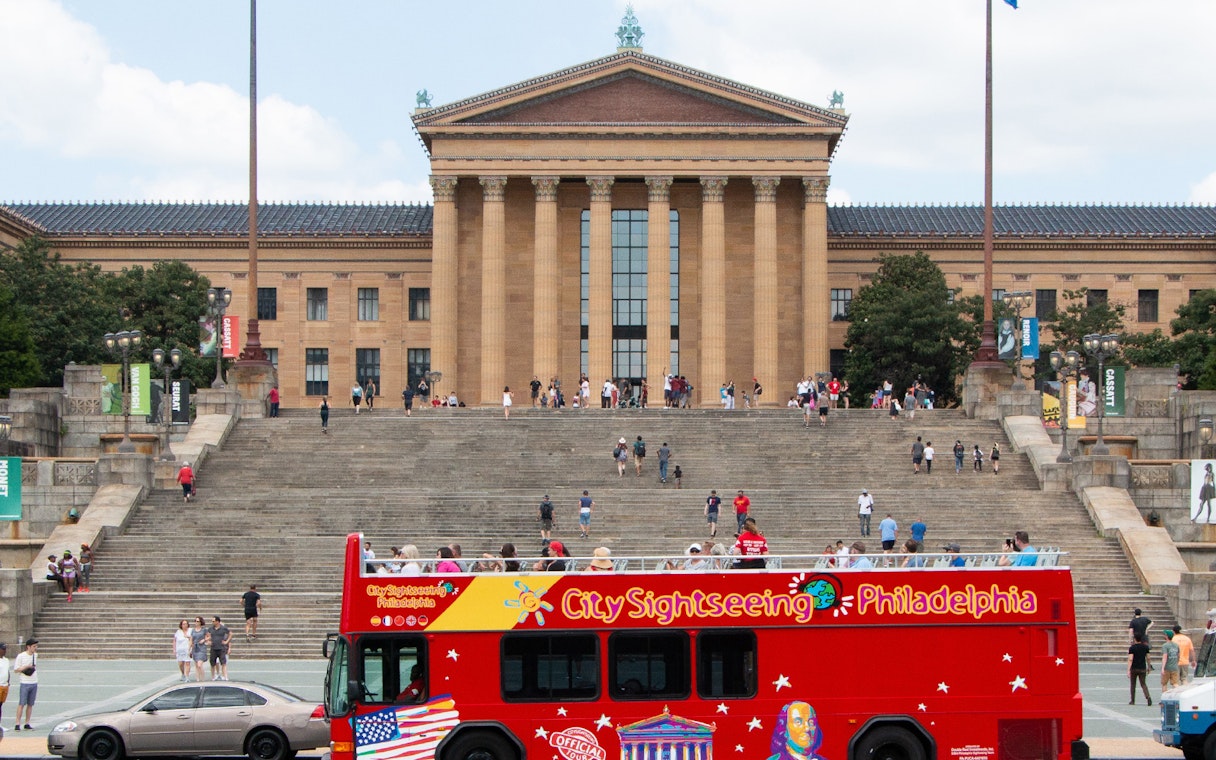 Red sightseeing bus in front of the Philadelphia Museum of Art steps on a hop-on-hop-off tour.