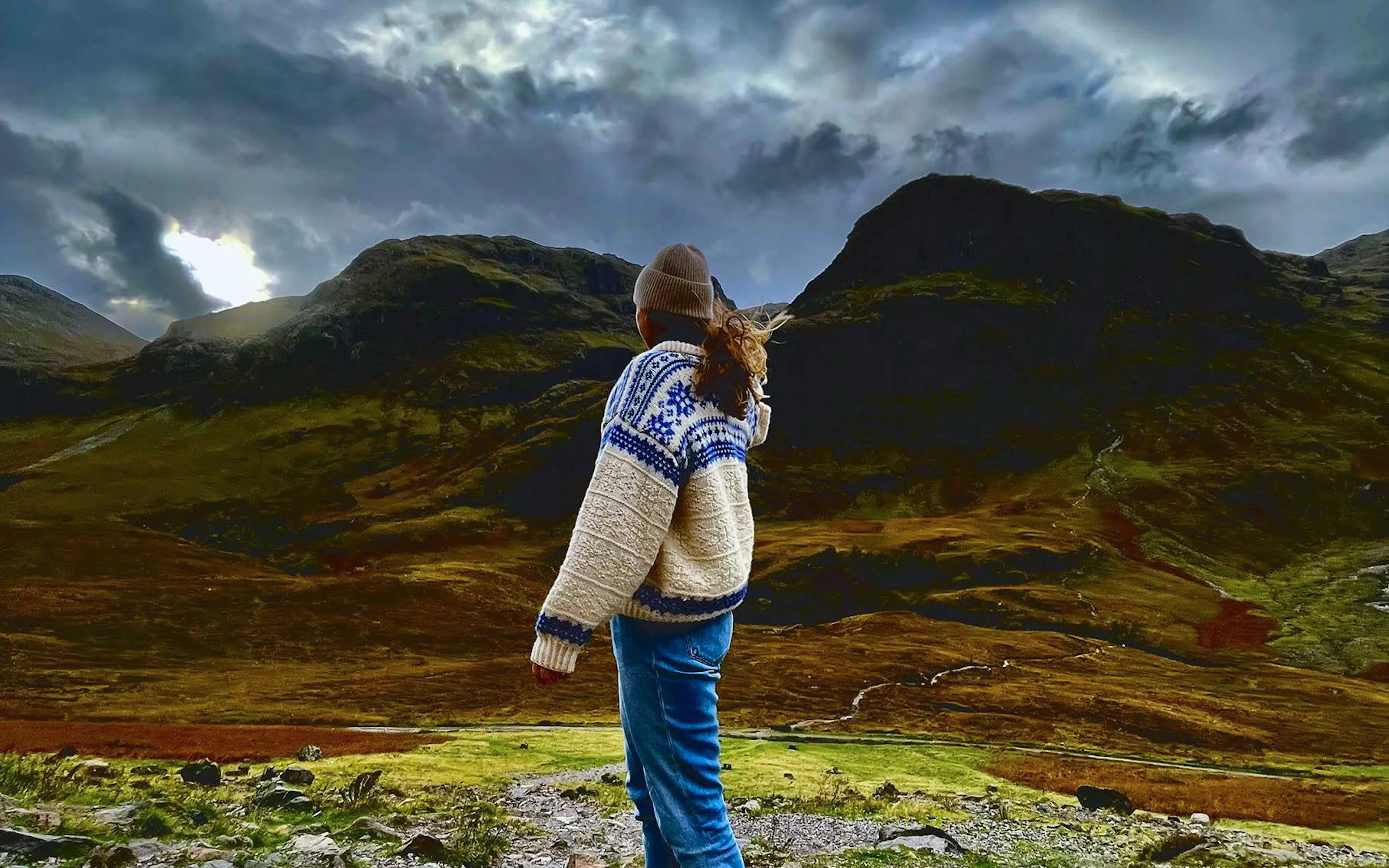 Person standing in Glencoe valley with dramatic mountain landscape.
