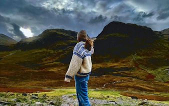 Person standing in Glencoe valley with dramatic mountain landscape.