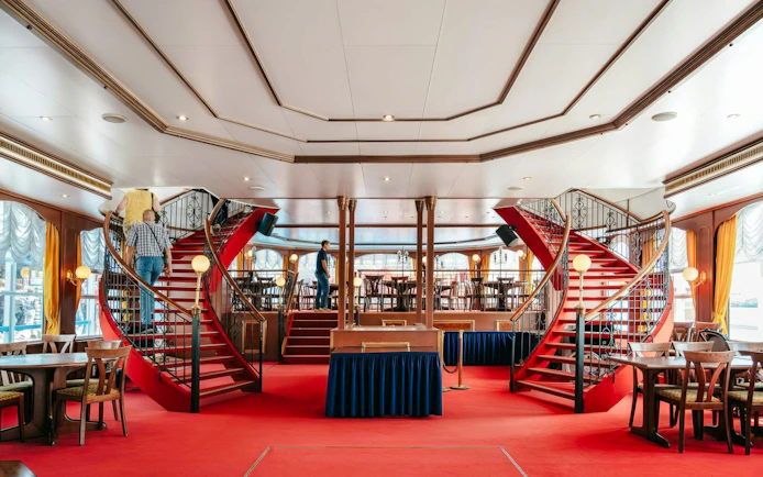 Interior of Hamburg Cruise with red carpeted stairs and dining area.