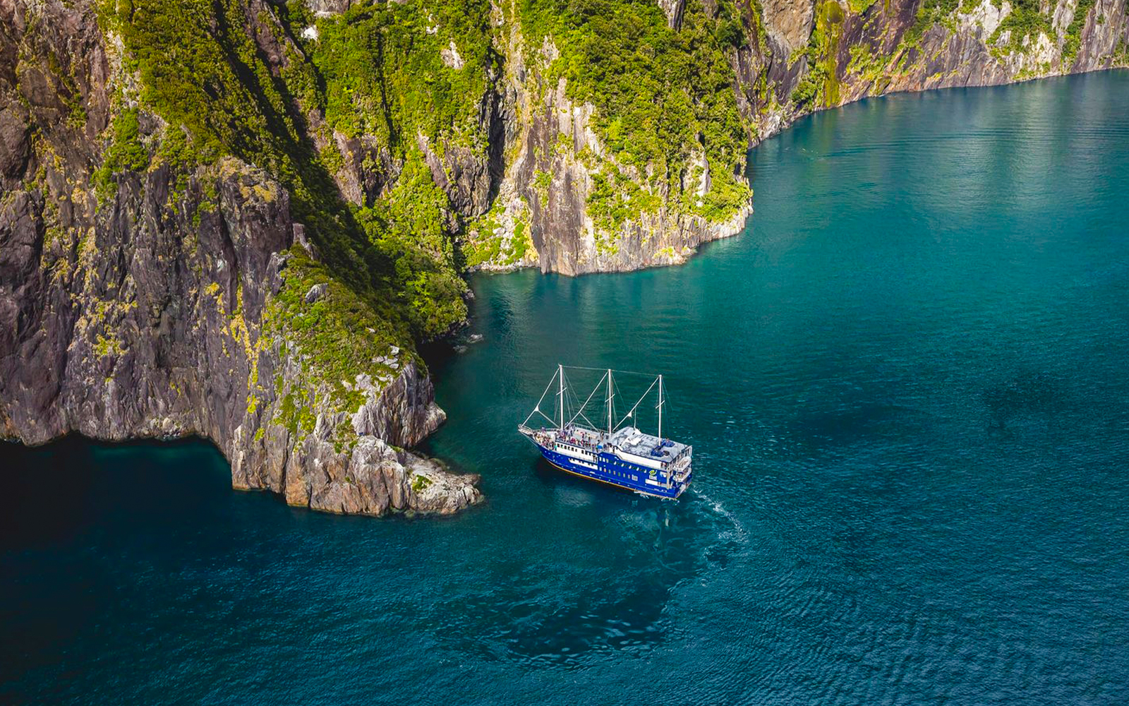 Cruise ship navigating Milford Sound's cliffs and blue waters, New Zealand.