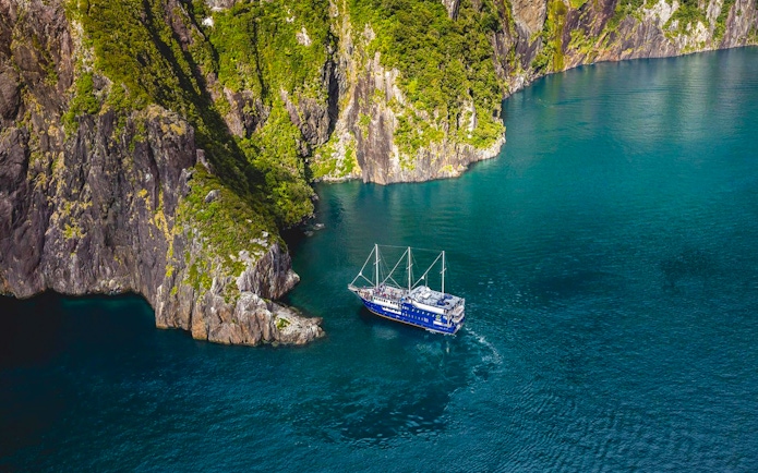 Cruise ship navigating Milford Sound's cliffs and blue waters, New Zealand.