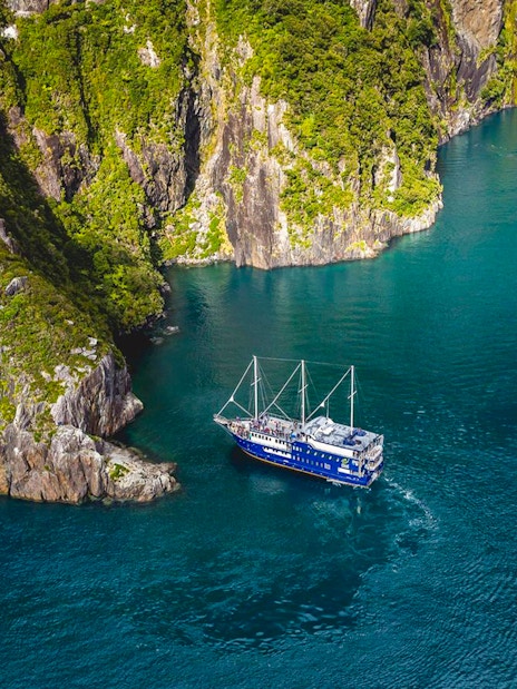 Cruise ship navigating Milford Sound's cliffs and blue waters, New Zealand.