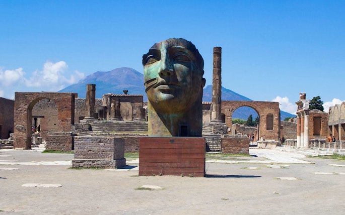 Ancient Pompeii ruins with large sculpture and Mount Vesuvius in background, Naples, Italy.