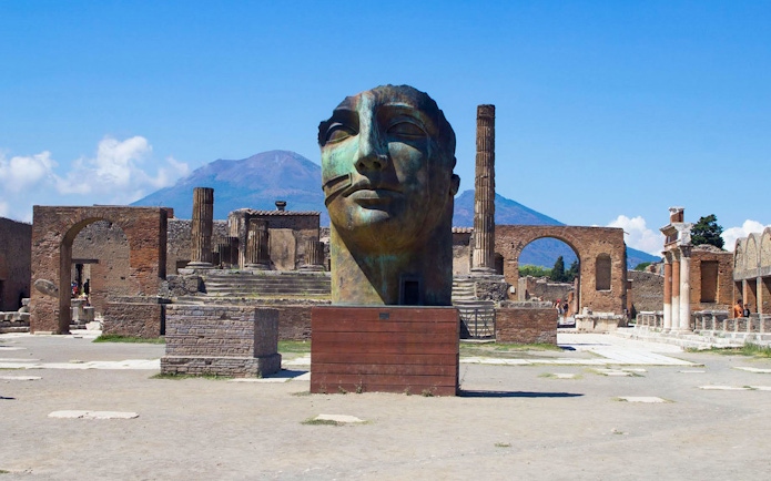 Ancient Pompeii ruins with large sculpture and Mount Vesuvius in background, Naples, Italy.