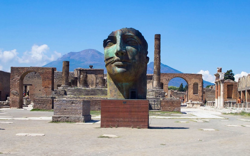 Ancient Pompeii ruins with large sculpture and Mount Vesuvius in background, Naples, Italy.