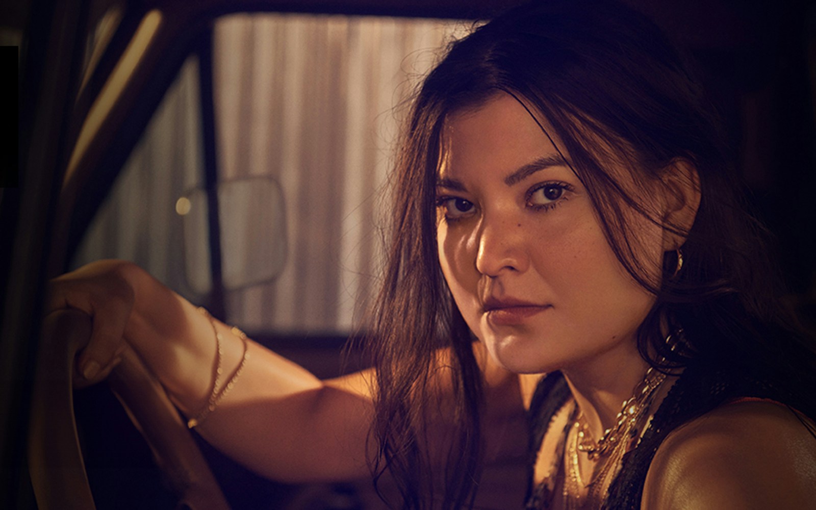 Woman sitting in a dimly lit car, looking intently at the camera, related to Carmen.