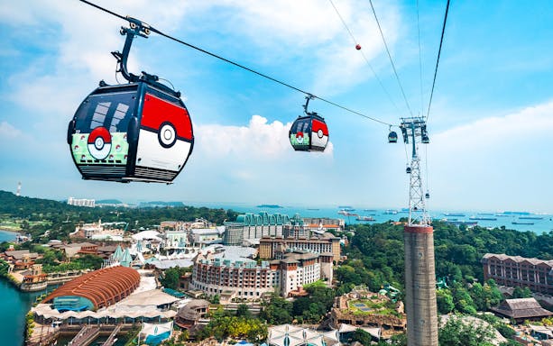 Cable cars with themed designs traveling over Sentosa Island, Singapore, with a view of the coastline.