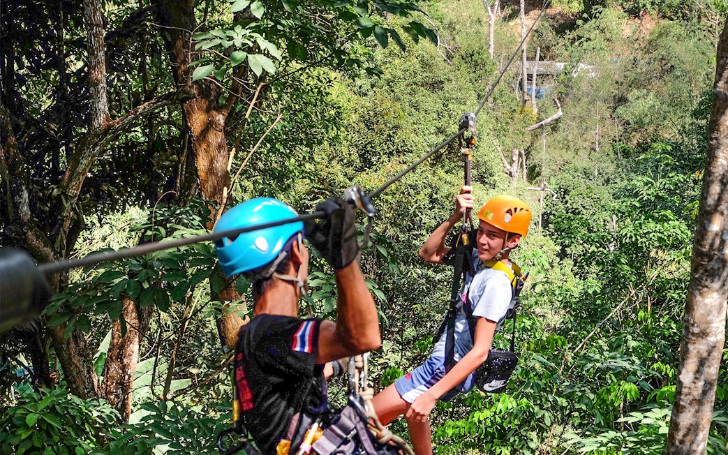 Two people ziplining through lush forest at Phuket Paradise.