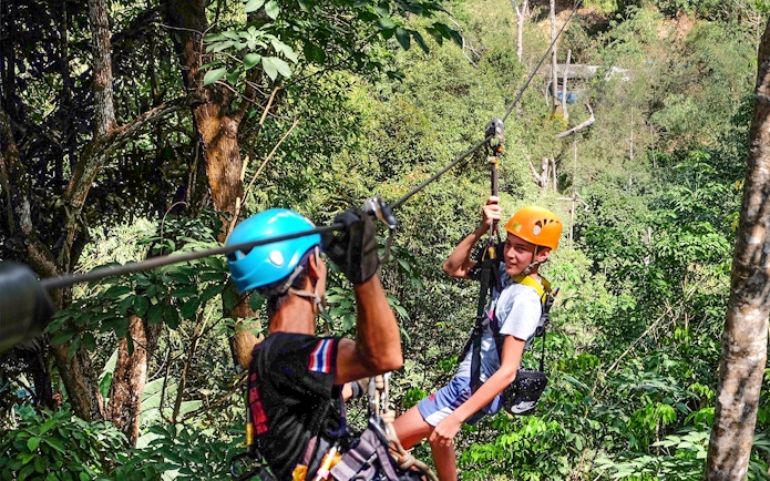 Two people ziplining through lush forest at Phuket Paradise.