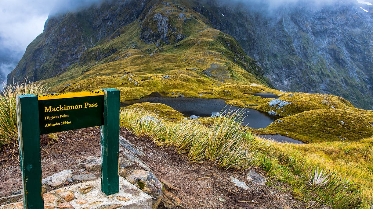 Mackinnon Pass sign with mountain view on Milford Track, New Zealand.