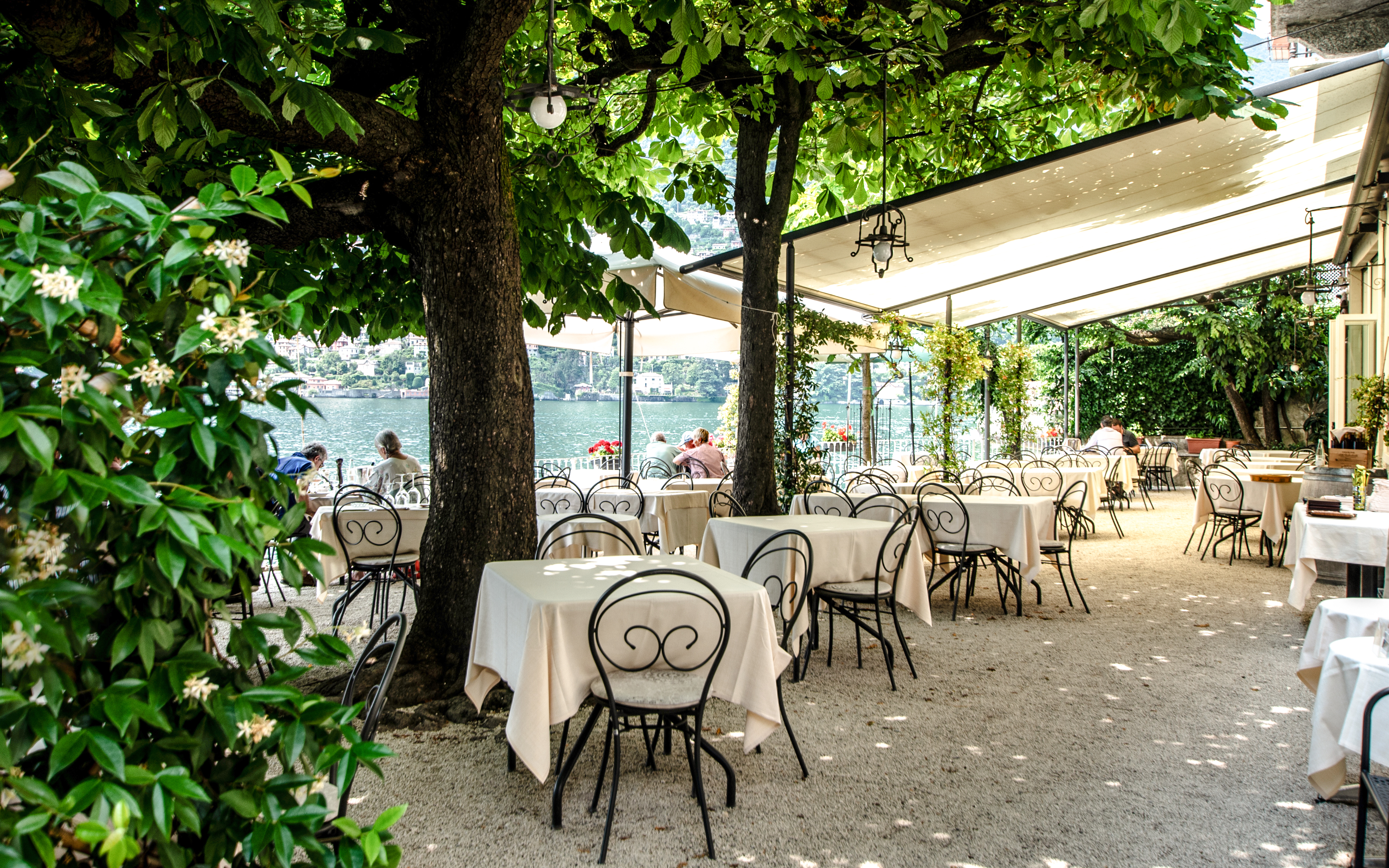 Outdoor restaurant with lake view in Stresa, tables under trees.