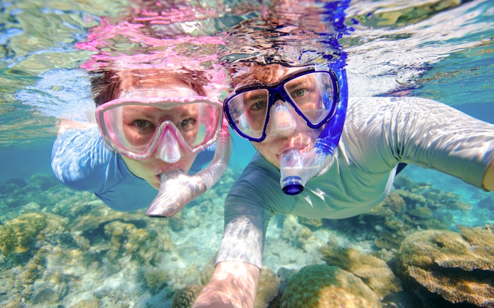 Couple snorkeling near coral reefs in clear waters, Oahu, Hawaii.